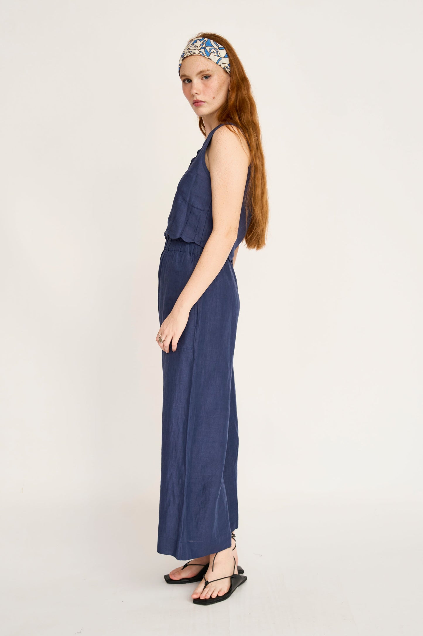 Woman with long red hair in a blue cotton top, sandals, and headband, shown in profile.