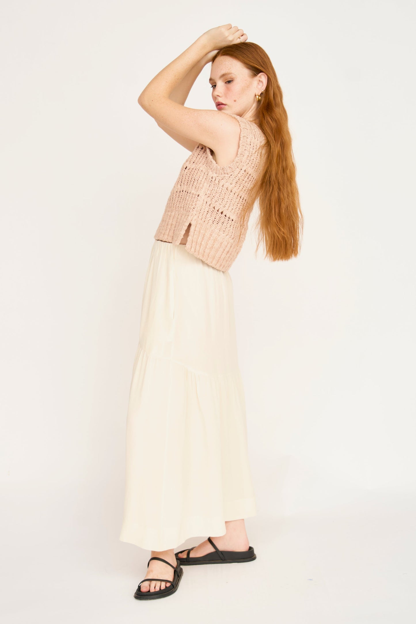 Woman with long red hair models a sleeveless knit top and cream silk skirt against a plain white background.