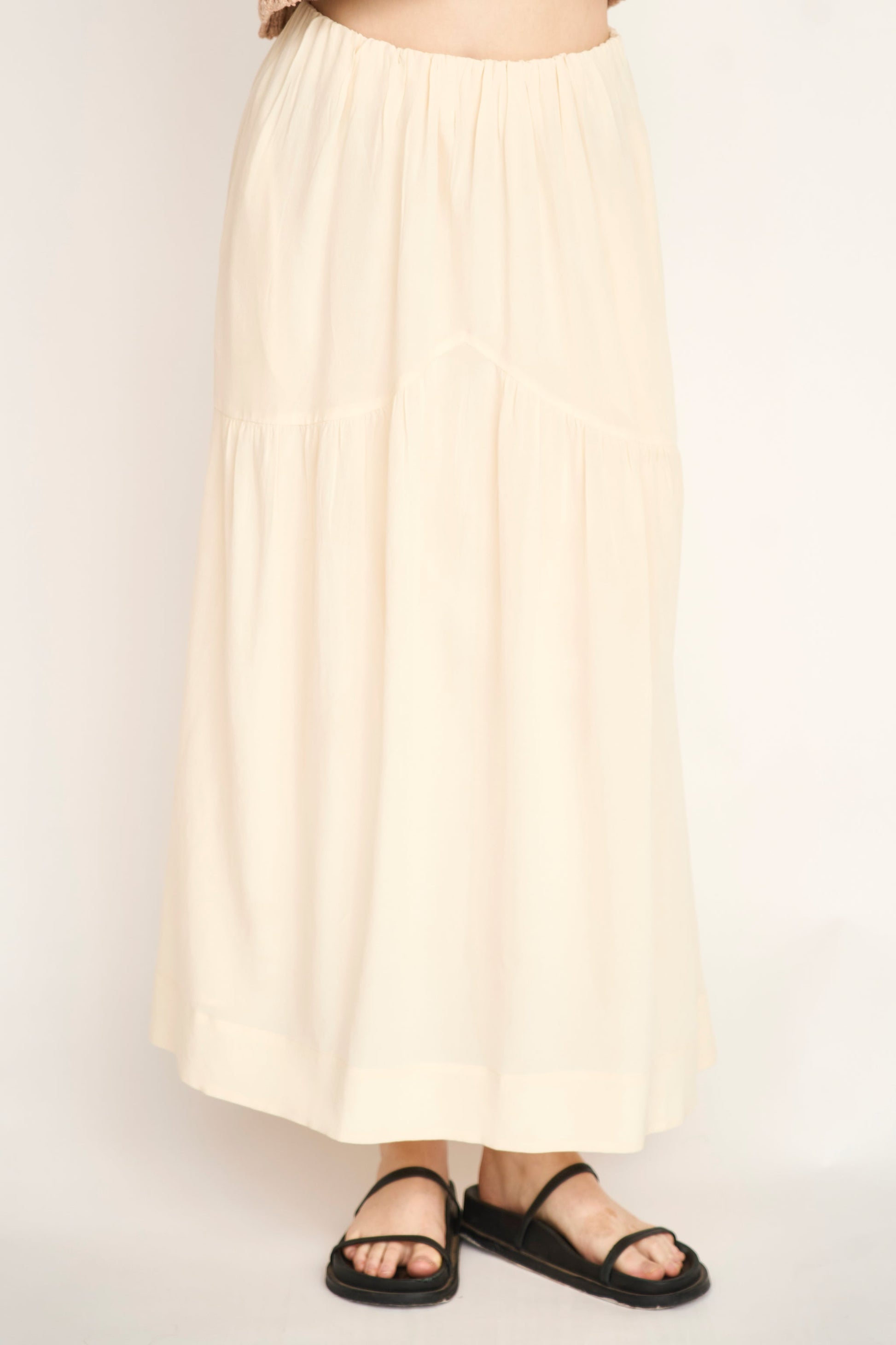 Cream silk skirt with black sandals, shown on a model standing against a plain light background.