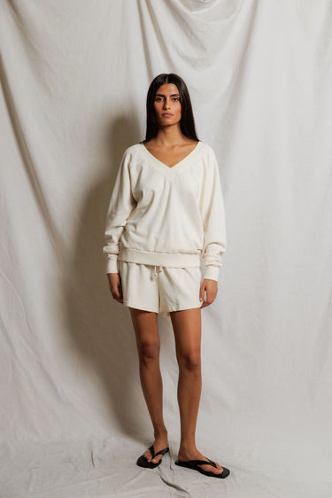 Woman wearing an ivory v-neck sweater and sweat shorts