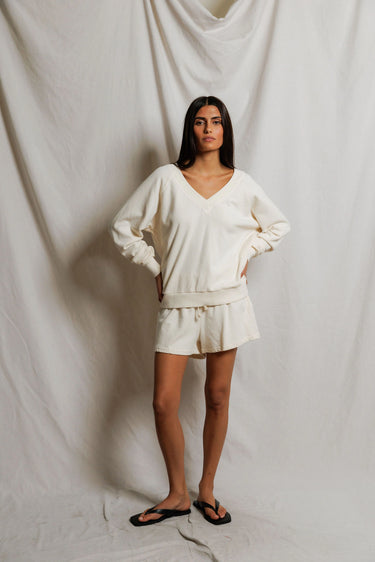 Woman wearing an ivory v-neck sweater and sweat shorts