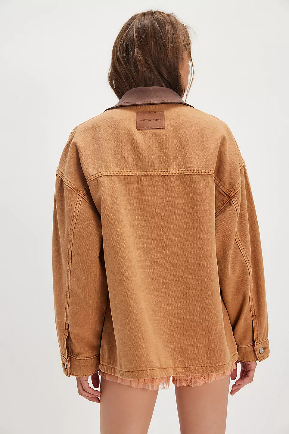 Woman with long brown hair wears a yellow denim jacket, standing against a plain background.