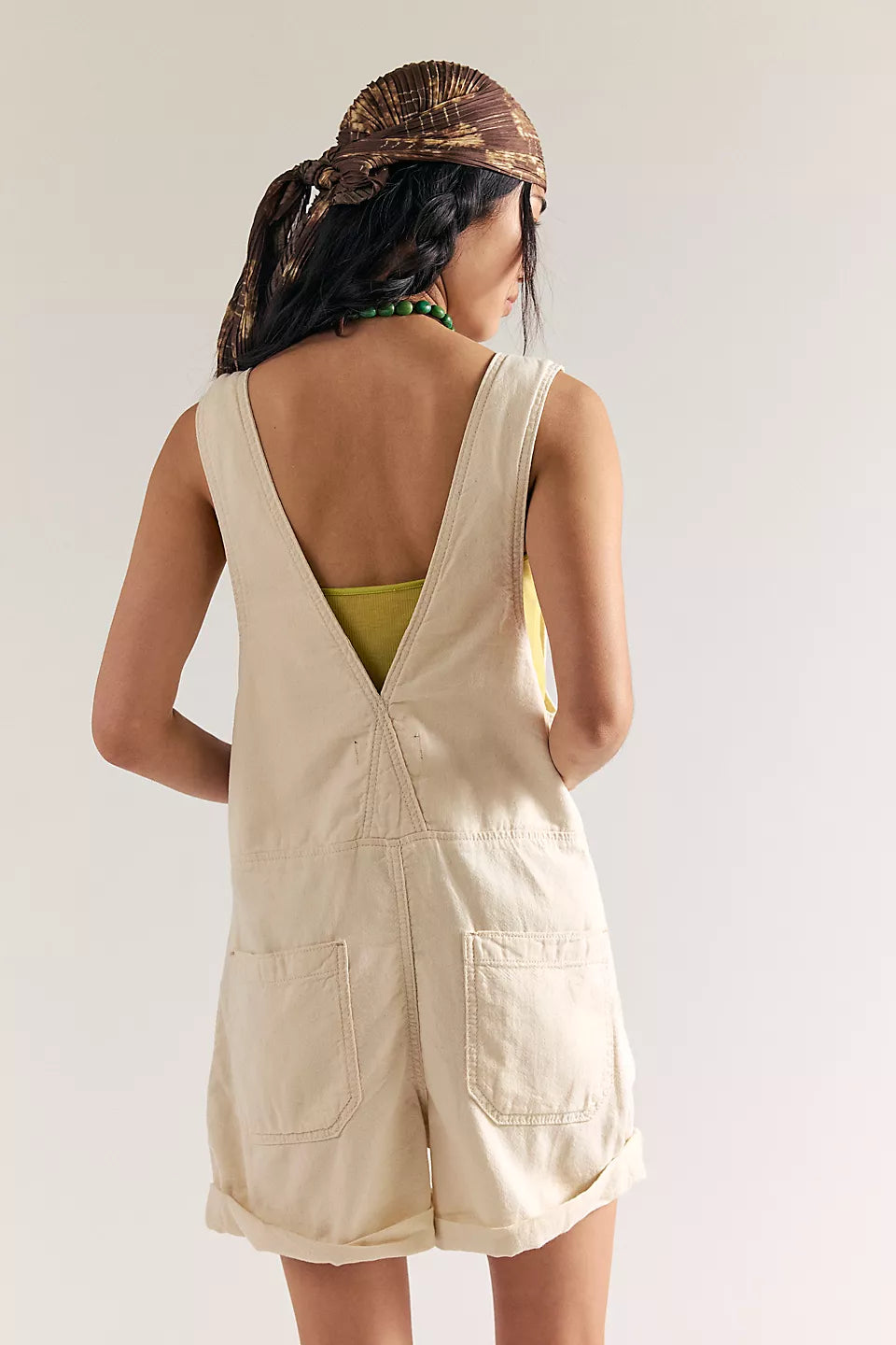 Woman wearing an ecru colored short denim overalls