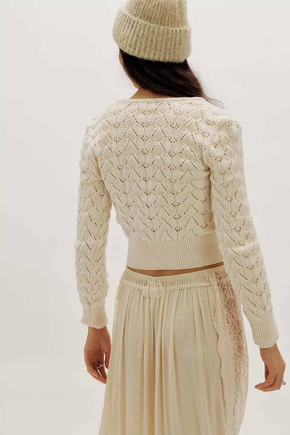 Back view of woman in ivory pointelle knit cardigan, matching skirt, and beanie.