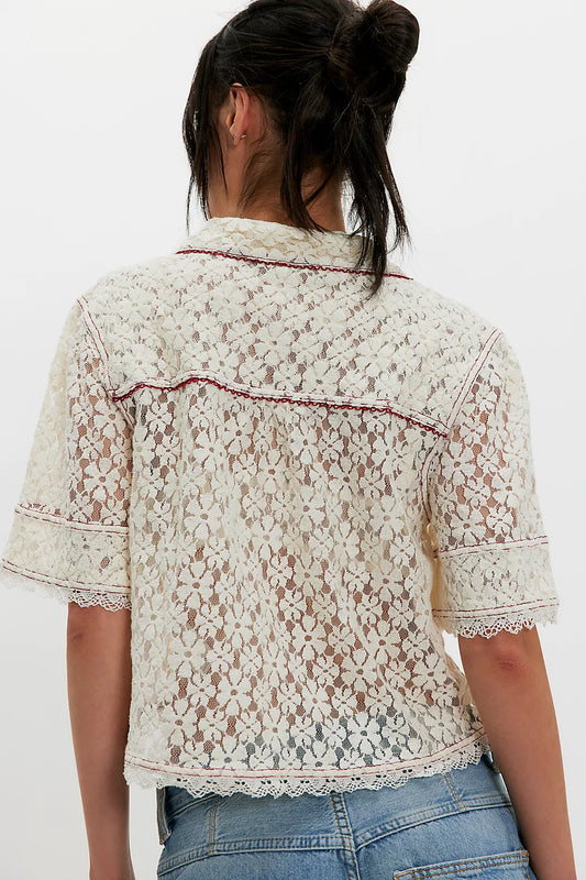 Woman with dark hair in a bun wears a white lace button-down shirt and light blue jeans, shown from the back.