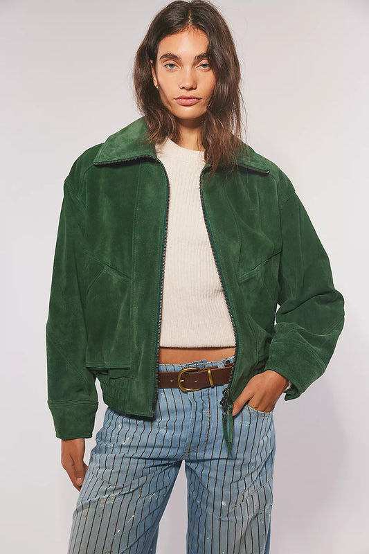 Woman wears a green suede jacket, cream sweater, and striped blue jeans.