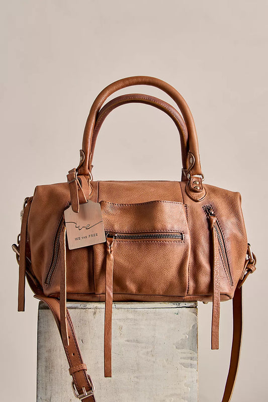 Tan leather tote with double handles, front zippers, and tag, displayed on a wooden surface.