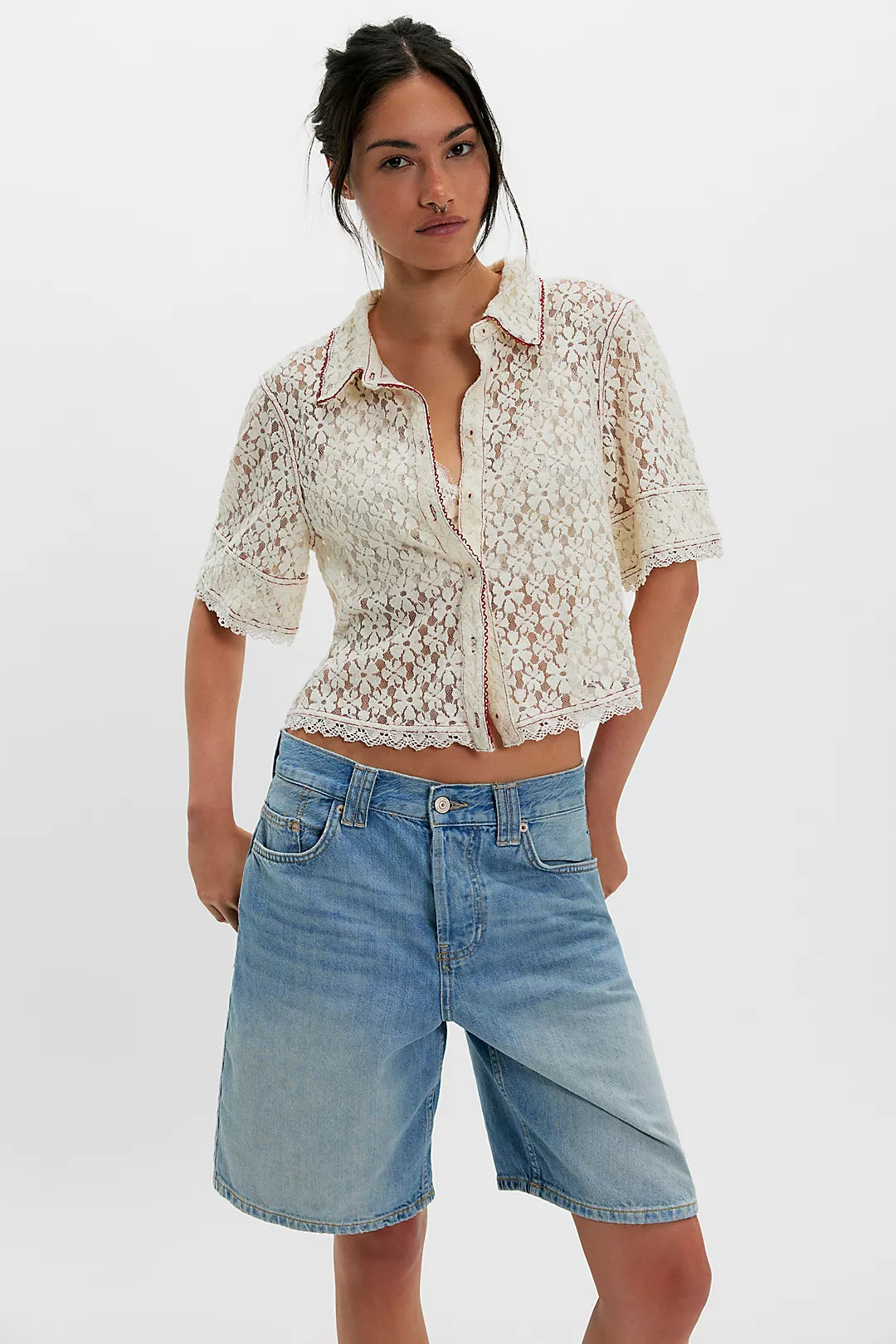 Woman in white lace button-down shirt and knee-length denim shorts, posed against a plain white background.