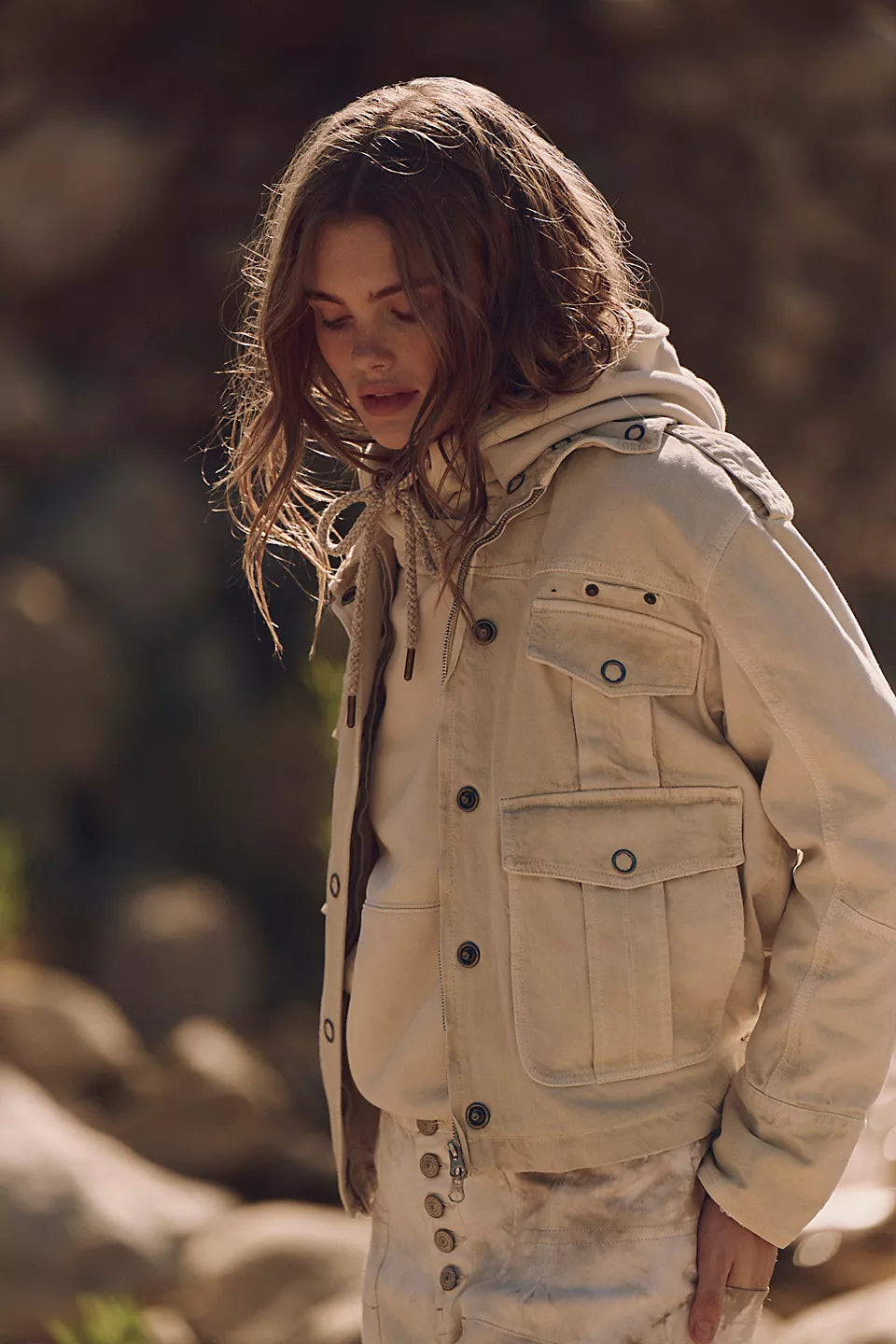 Woman outdoors in a light beige washed cotton jacket, head down, loose hair framing her face.