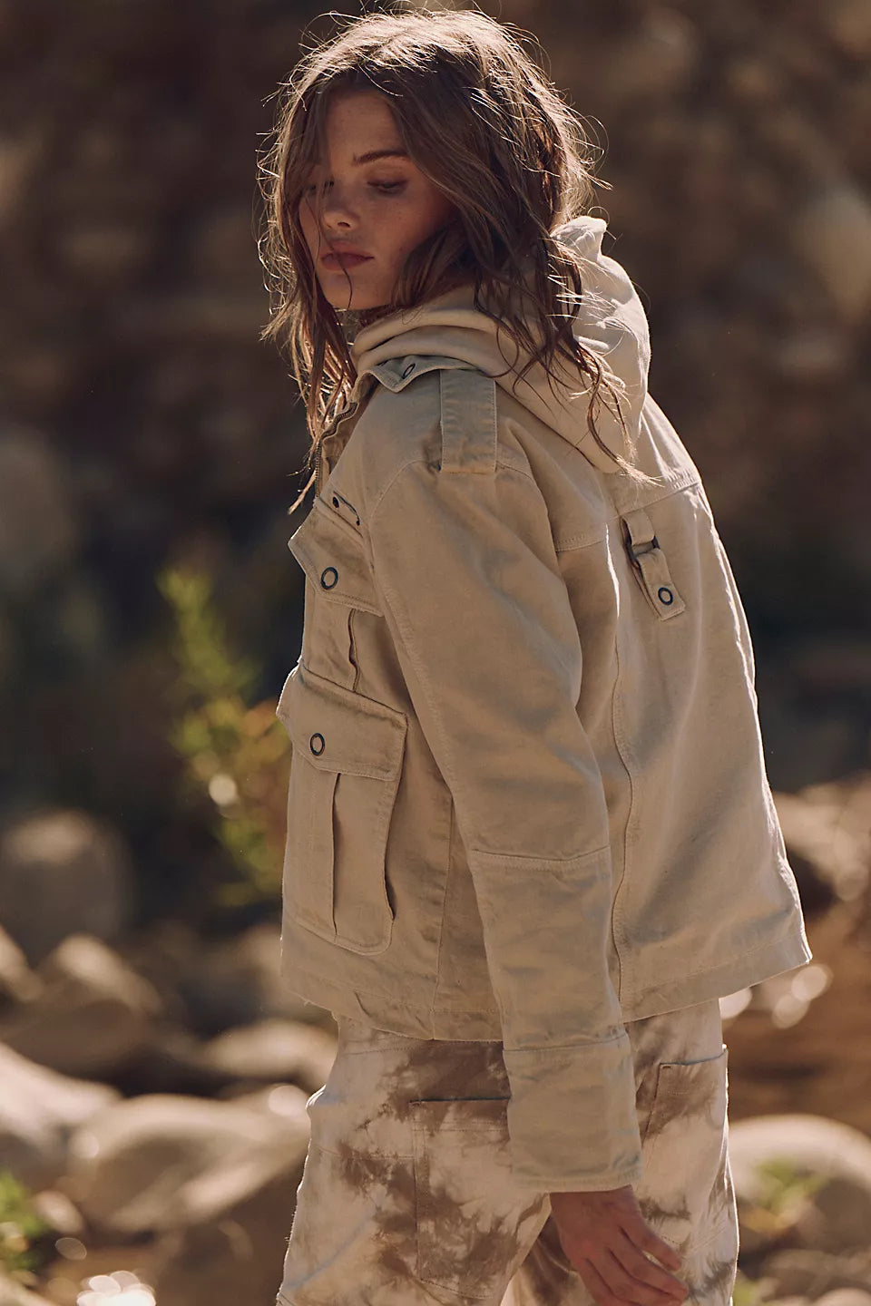 Woman outdoors in sunlight wearing a light beige washed denim jacket, looking down.