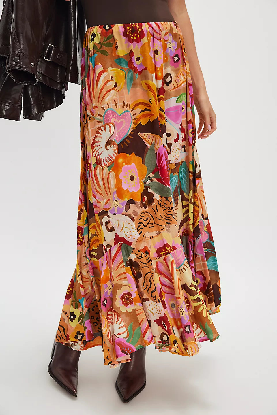 Person wearing a caramel maxi skirt with brown heeled boots, holding a dark jacket.