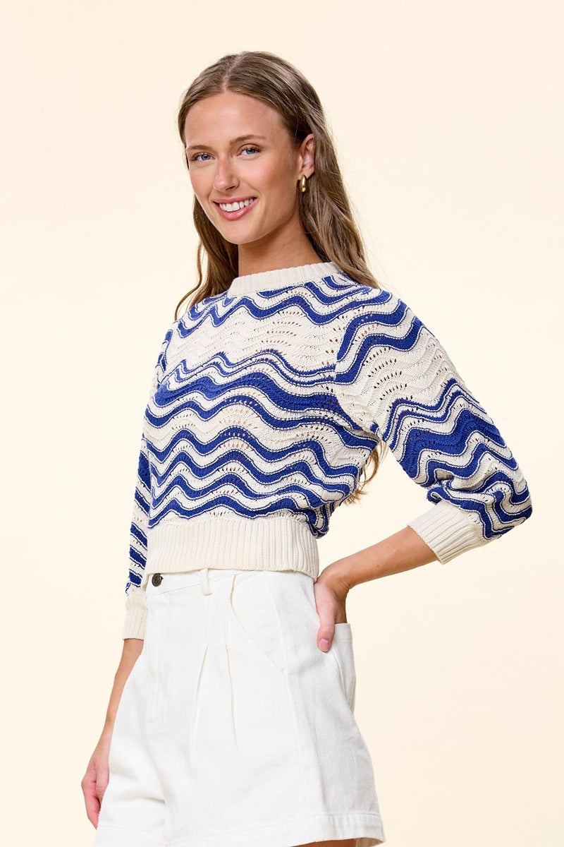 A woman modeling a blue and cream wavy knit sweater